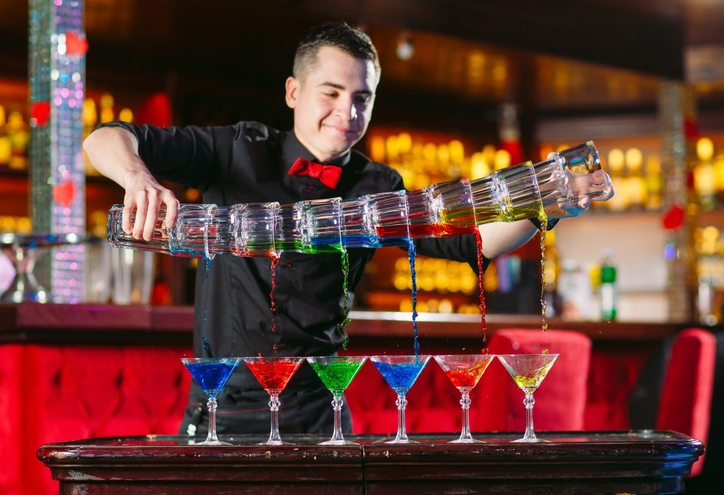 Barman wykonuje pokaz barmański i nalewa koktajle do szklanek.